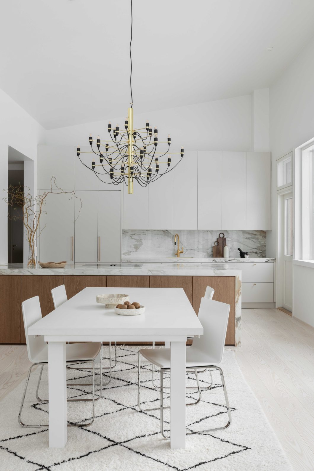 Moderni designkeittiö, jossa hiekan sävyinen mulperi-maalattu kaapisto, marmorikuvioinen keraaminen työtaso ja välitila sekä tummasta tammiviilusta tehty keittiösaareke.
