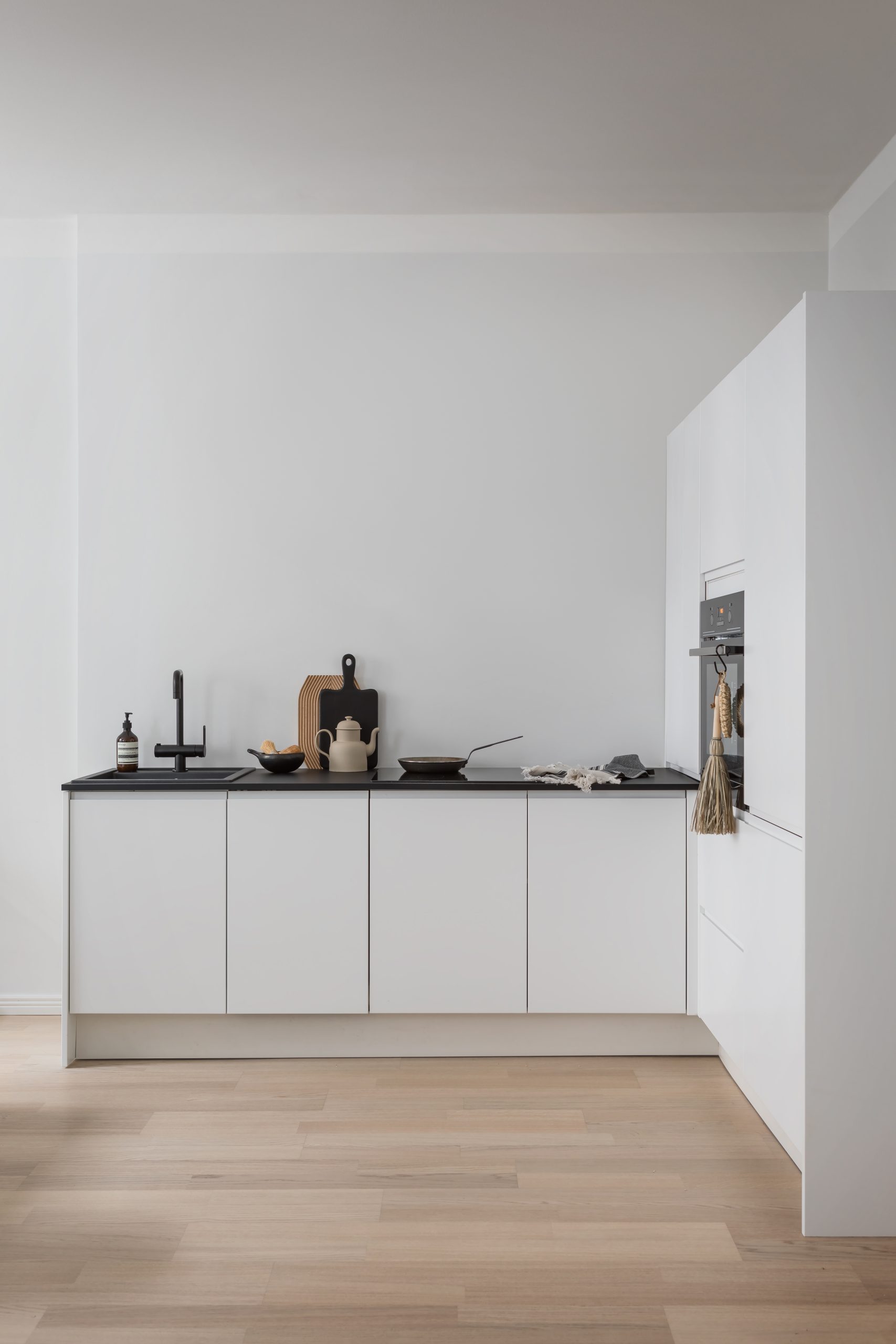 Blau minimalistinen valkoinen keittiö mustilla tasoilla ja hanalla