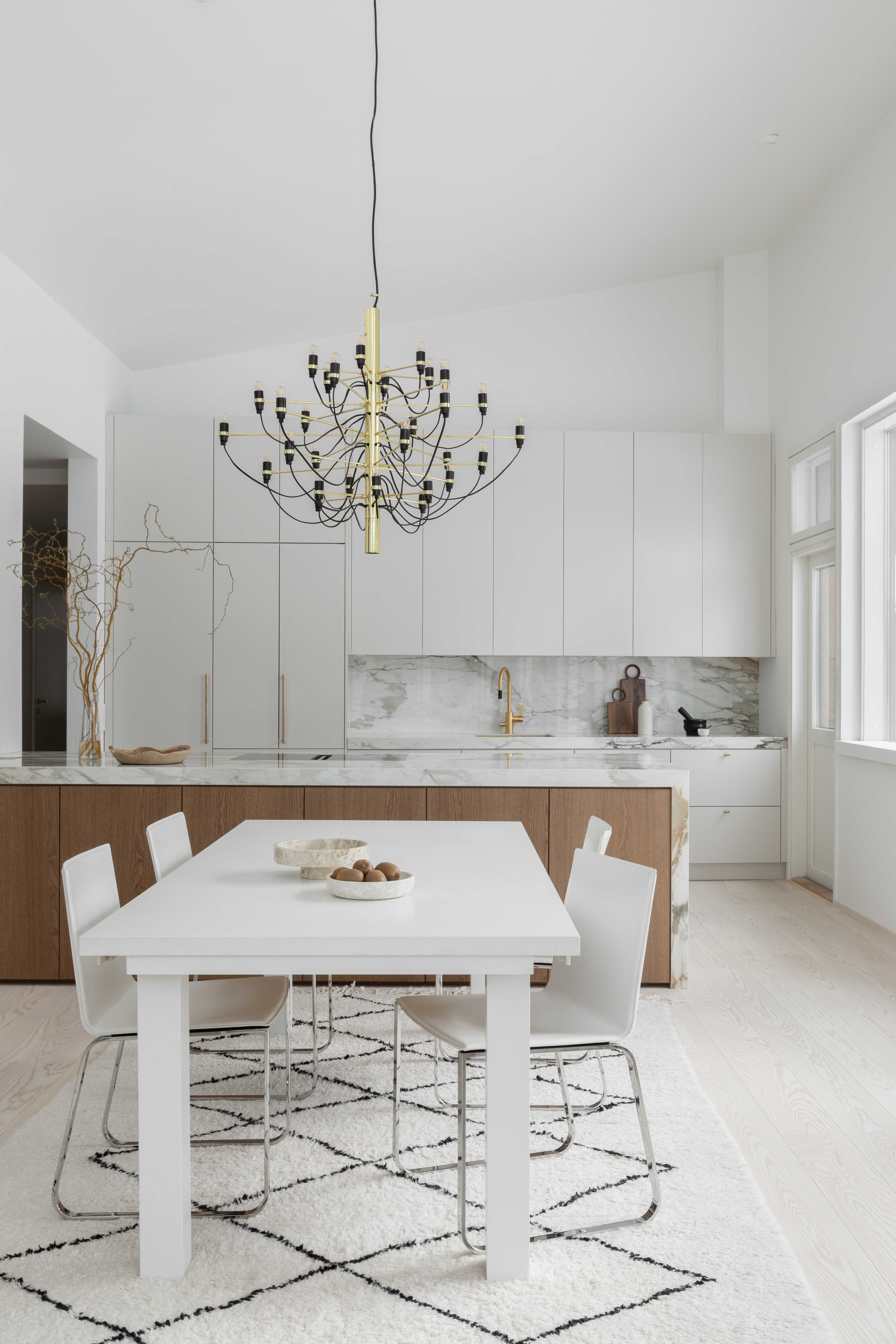 Moderni designkeittiö, jossa hiekan sävyinen mulperi-maalattu kaapisto, marmorikuvioinen keraaminen työtaso ja välitila sekä tummasta tammiviilusta tehty keittiösaareke.