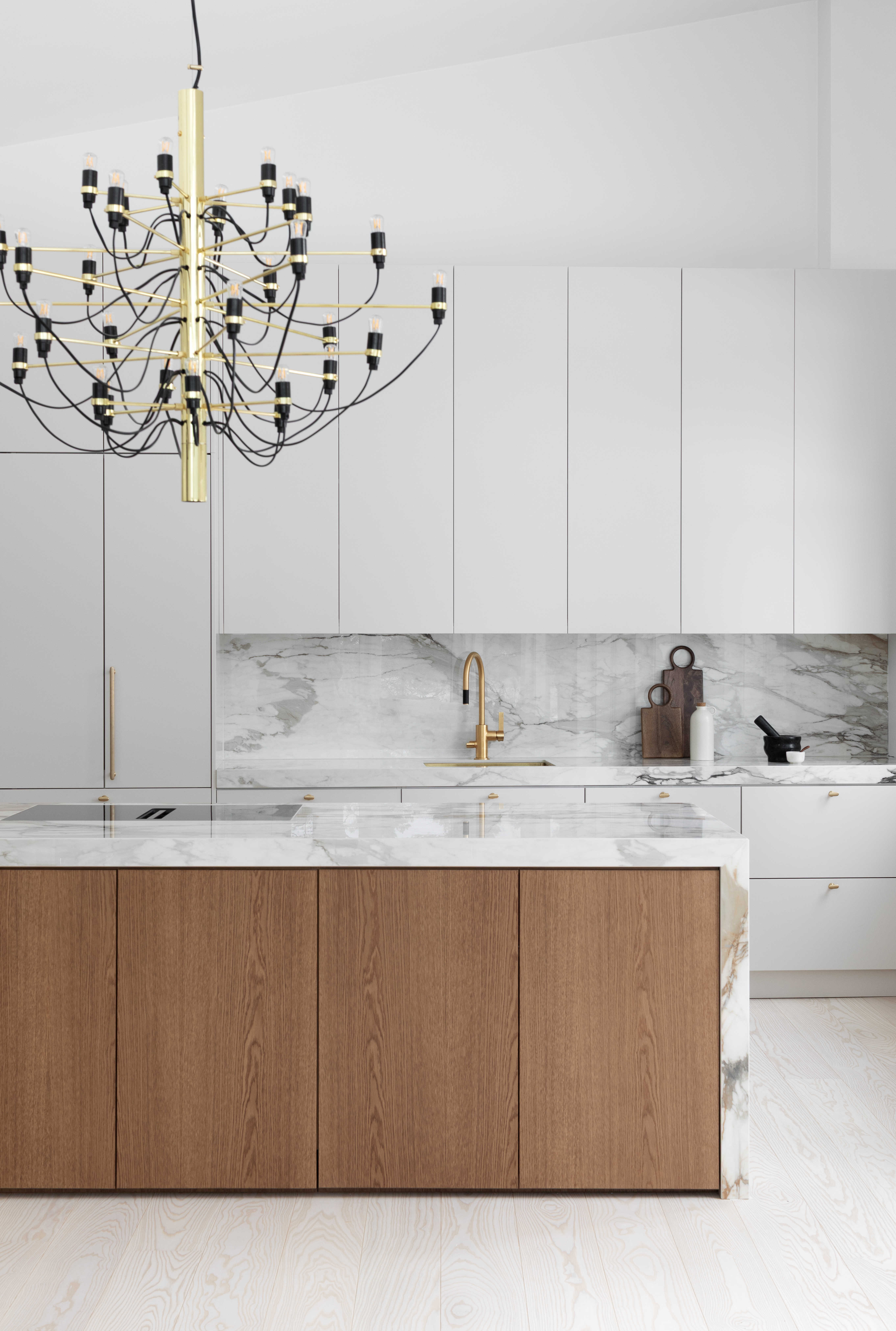 Moderni designkeittiö, jossa hiekan sävyinen mulperi-maalattu kaapisto, marmorikuvioinen keraaminen työtaso ja välitila sekä tummasta tammiviilusta tehty keittiösaareke.