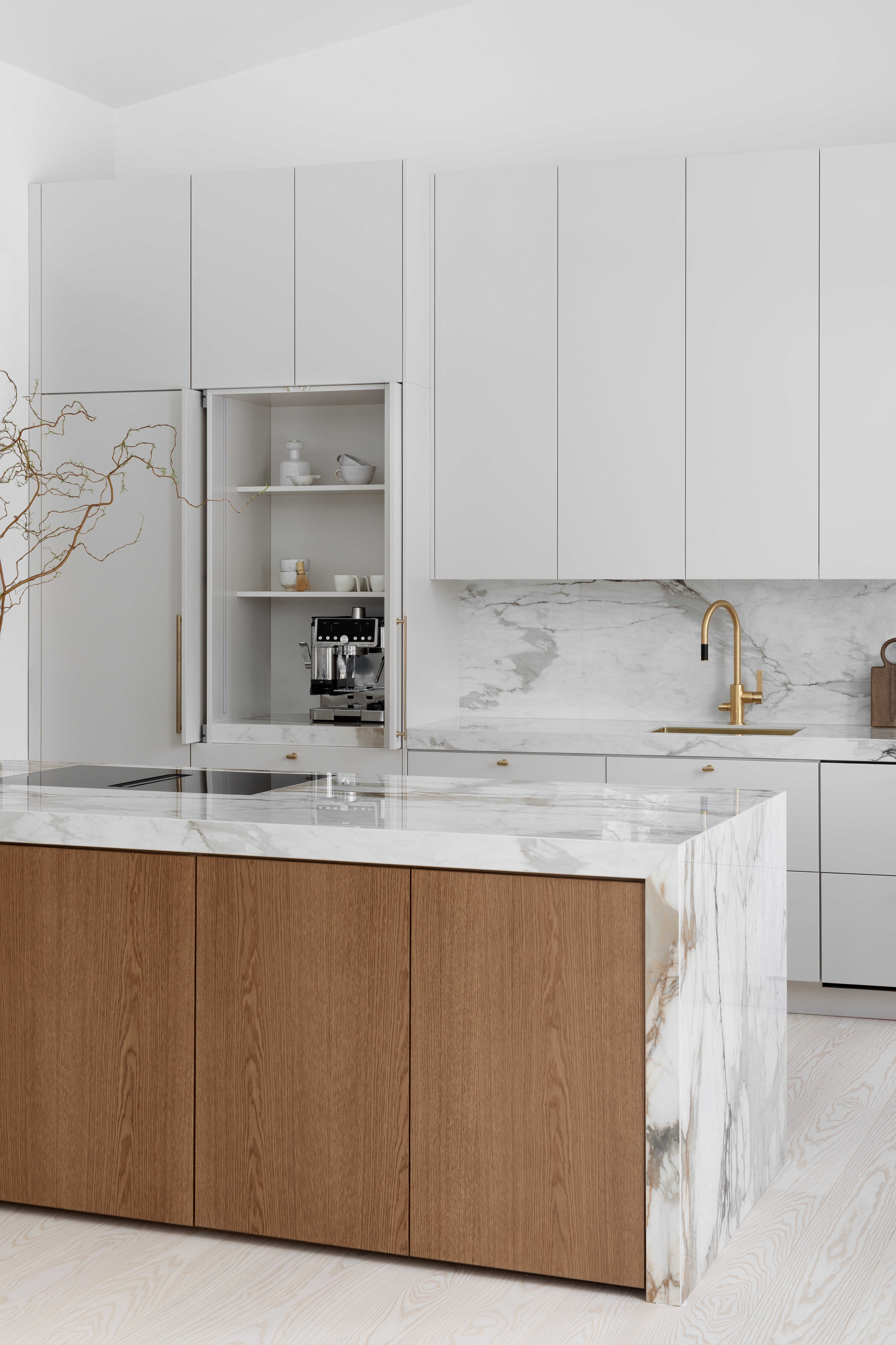 Moderni designkeittiö, jossa hiekan sävyinen mulperi-maalattu kaapisto, marmorikuvioinen keraaminen työtaso ja välitila sekä tummasta tammiviilusta tehty keittiösaareke.
