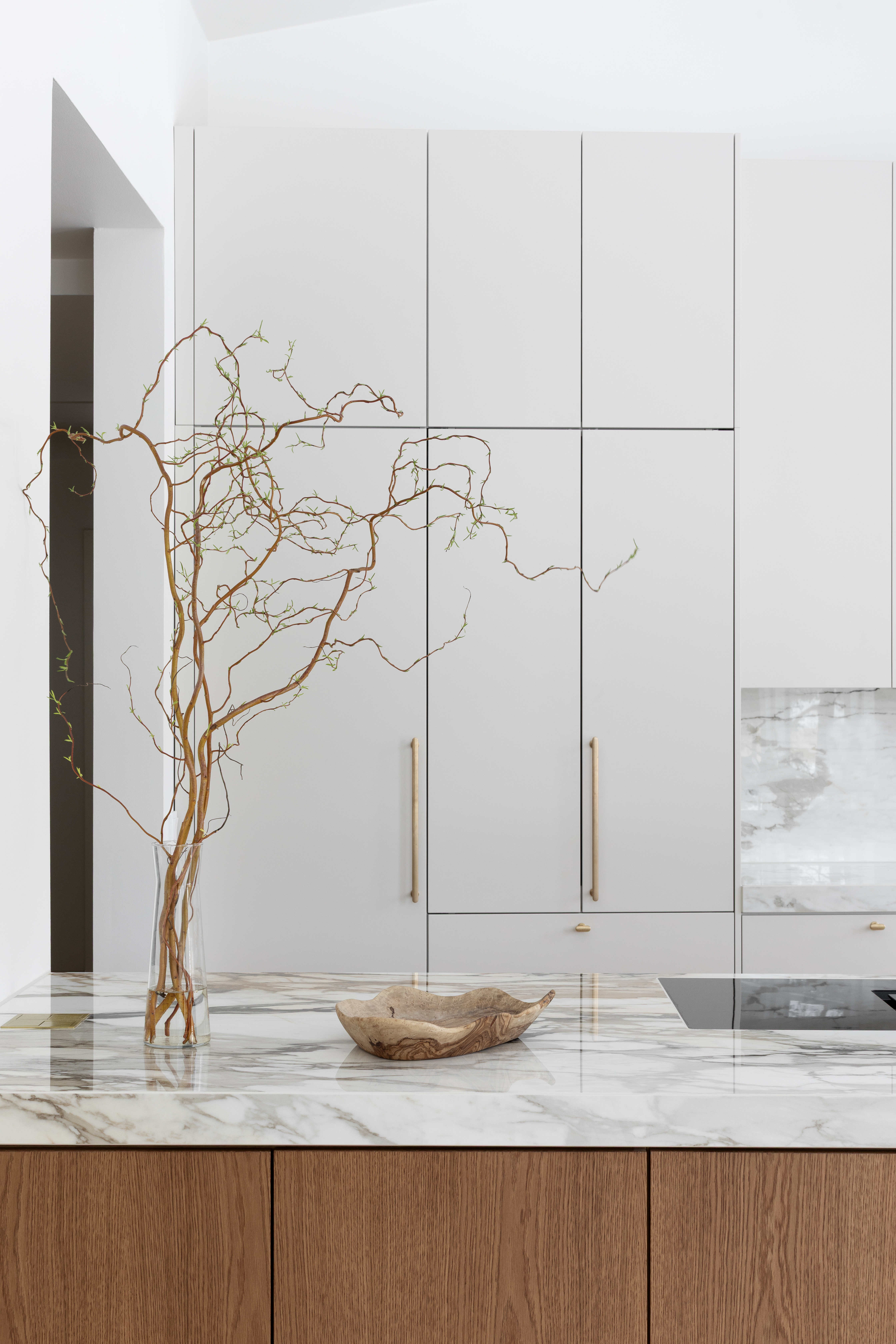 Moderni designkeittiö, jossa hiekan sävyinen mulperi-maalattu kaapisto, marmorikuvioinen keraaminen työtaso ja välitila sekä tummasta tammiviilusta tehty keittiösaareke.